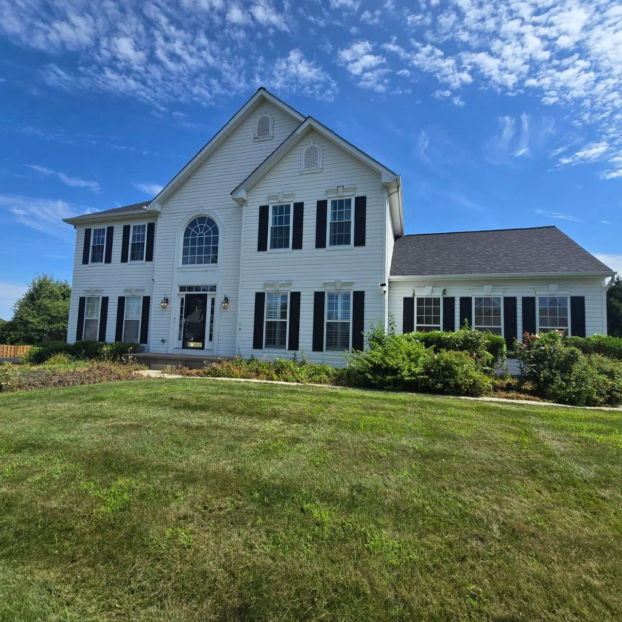 White colonial home with black shutters and an arched entry window under a blue sky